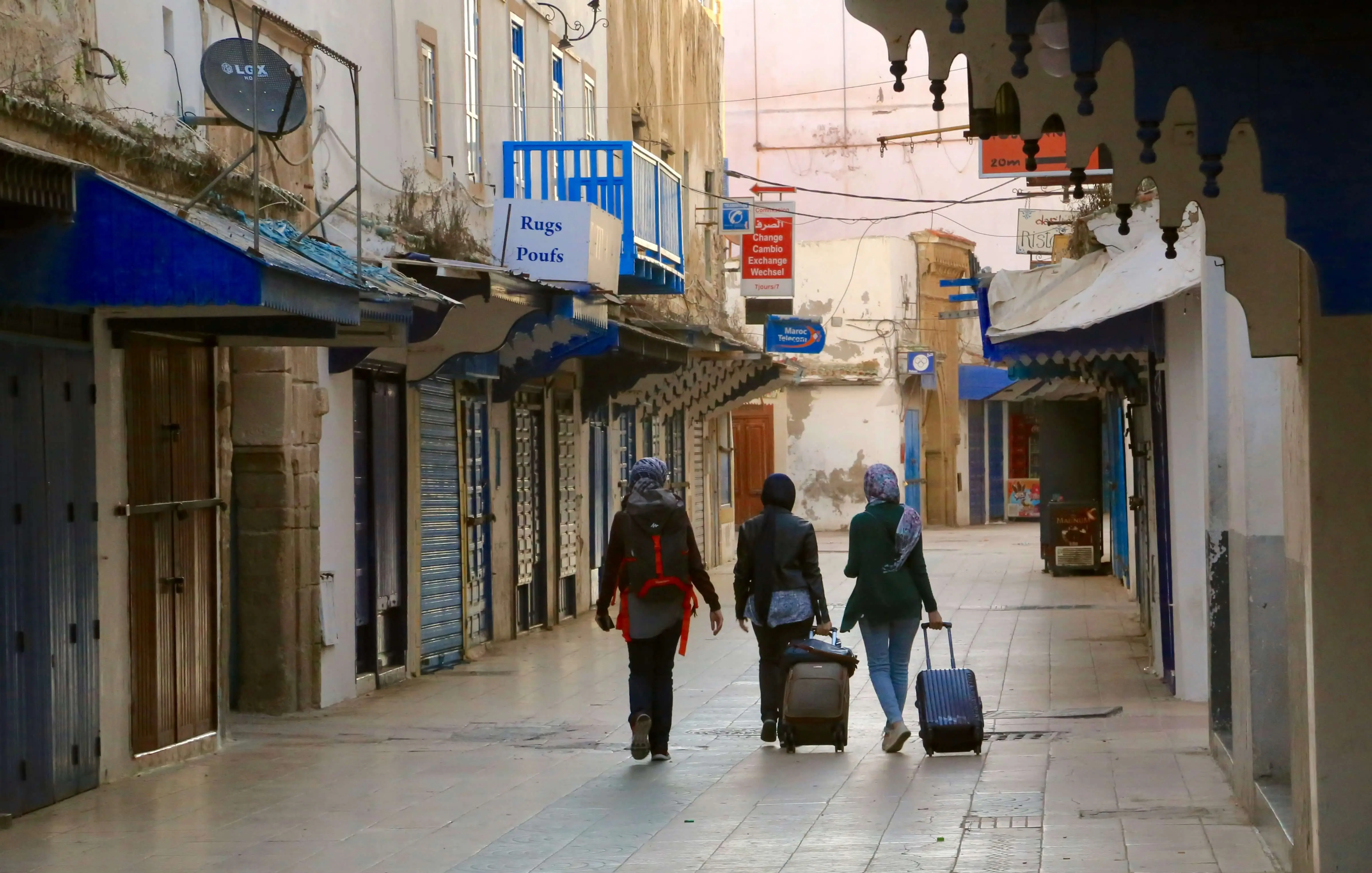 Travel suitcase packed with colorful clothing, traditional Moroccan items, and travel essentials laid out on bed